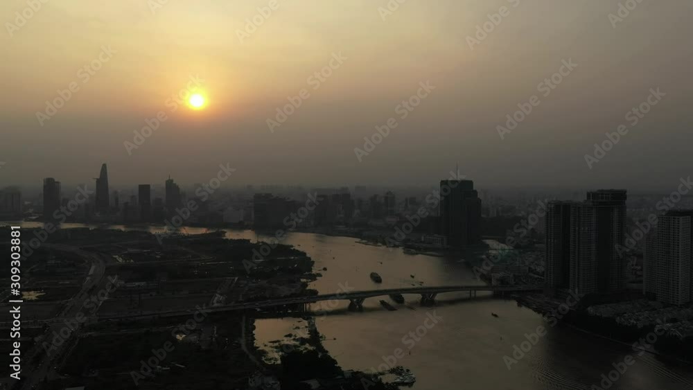 Drone shot of Saigon river smoggy sunset typical of a day with an extreme air pollution reading in Southeast Asia. Slow fly in towards bridge, city skyline showing boat activity Drone shot of Saigon river smoggy sunset typical of a day with an extreme air pollution reading in Southeast Asia. Slow fly in towards bridge, city skyline showing boat activity