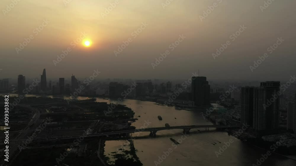 Drone shot of Saigon river smoggy sunset typical of a day with an extreme air pollution reading in Southeast Asia. Slow dolly shot moving across the river with city skyline and boat traffic Drone shot of Saigon river smoggy sunset typical of a day with an extreme air pollution reading in Southeast Asia. Slow dolly shot moving across the river with city skyline and boat traffic