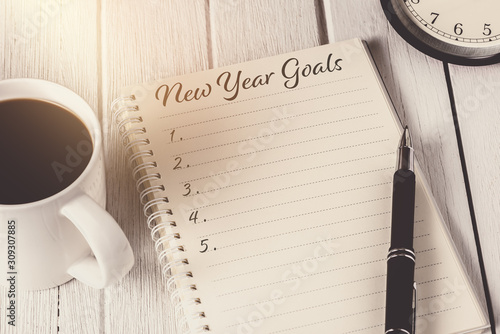 New Year's Goals List written on Notebook with alarm clock, pen, coffee