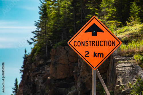 Construction work two kilometer ahead, Temporary condition road signs, close up selective focus on warning orange symbol with Rocky slope background