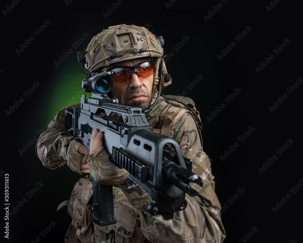 a male soldier in military clothes with a weapon on a dark background