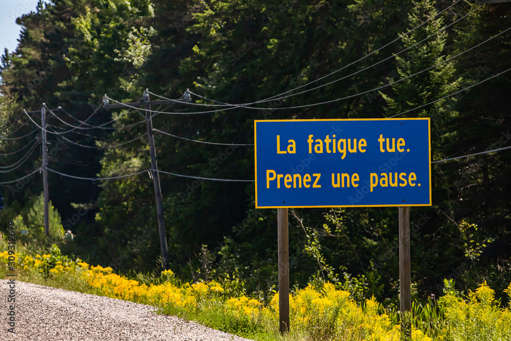 Blue Information Road Sign with french yellow writing, tiredness kills. take a break., on rural country roadside, trees background, Ontario, Canada