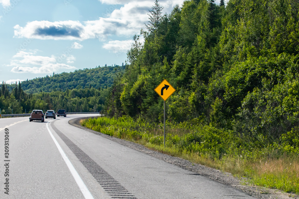 Vehicles on the road curve with warning slight bend or curve in the road  ahead to the right sign, a Canadian rural road between forests Stock Photo