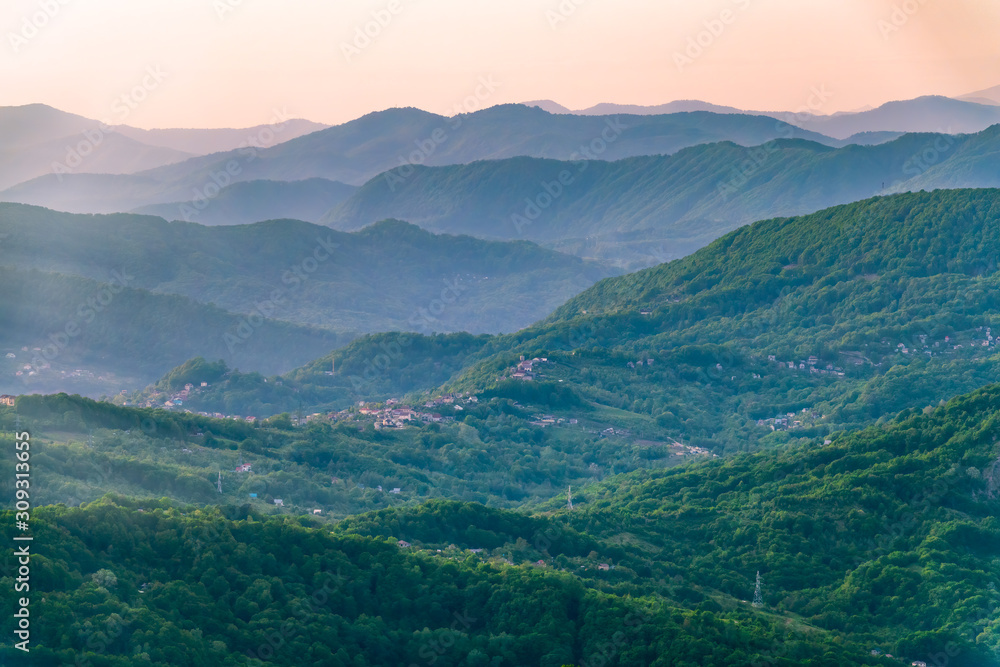 Layers of mountains in the haze during sunset. Beautiful sunset in the mountains. Beautiful sunset in a hilly valley with villages and fog in the lowlands.