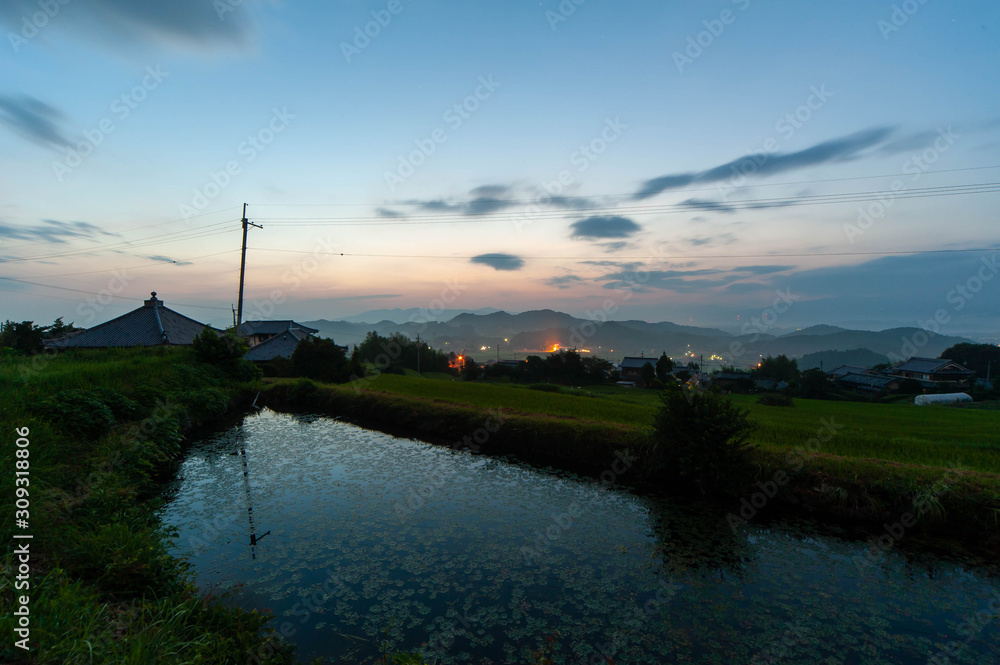 夜明けの空と農村の溜池