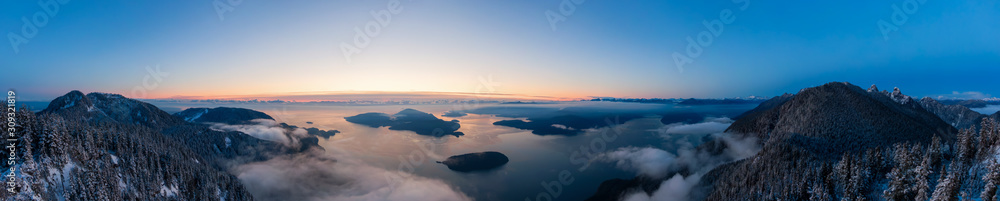 Fototapeta premium Aerial Panoramic View of Canadian Mountain Landscape on the Pacific Ocean Coast during a colorful sunset. Taken in Howe Sound near Vancouver, British Columbia, Canada.