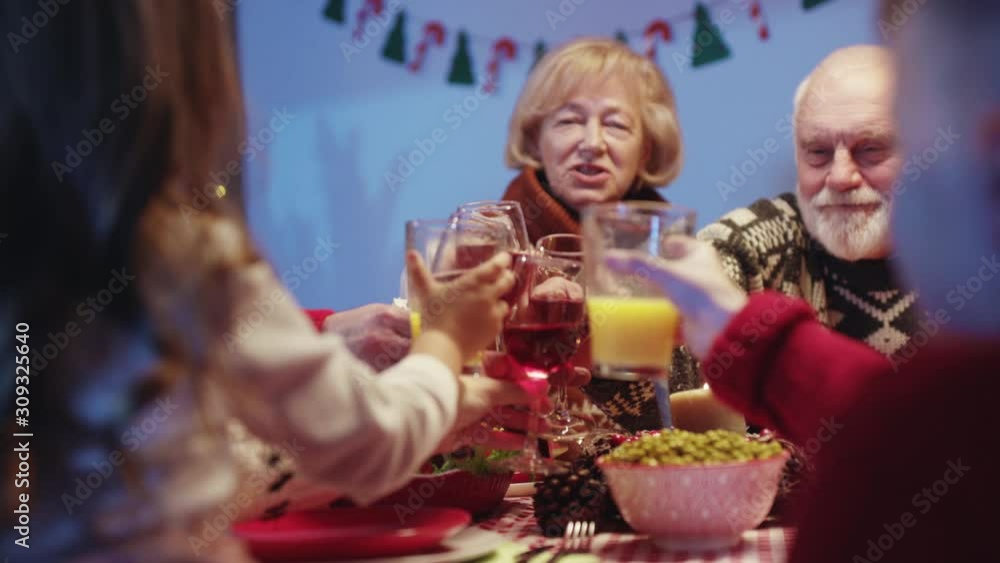 Cheerful grandparents toasting wine with family at Christmas dinner table greeting with New Year enjoying home feast celebrating winter holidays. Cheerful grandparents toasting wine with family at Christmas dinner table greeting with New Year enjoying home feast celebrating winter holidays.