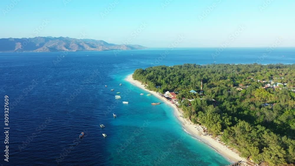 Idyllic tropical island for vacation gateway in Indonesia with lush vegetation and sandy exotic beach washed by blue turquoise lagoon full of anchored boats Idyllic tropical island for vacation gateway in Indonesia with lush vegetation and sandy exotic beach washed by blue turquoise lagoon full of anchored boats