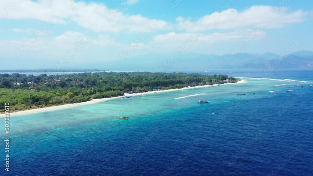 Idyllic tropical island with long white beach and lush vegetation, surrounded by calm clear water of turquoise lagoon on a bright sky background in Bali Idyllic tropical island with long white beach and lush vegetation, surrounded by calm clear water of turquoise lagoon on a bright sky background in Bali