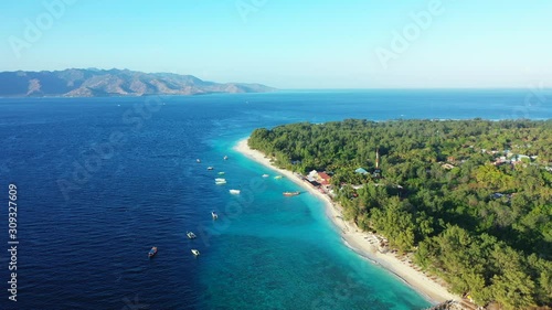 Idyllic tropical island for vacation gateway in Indonesia with lush vegetation and sandy exotic beach washed by blue turquoise lagoon full of anchored boats photo