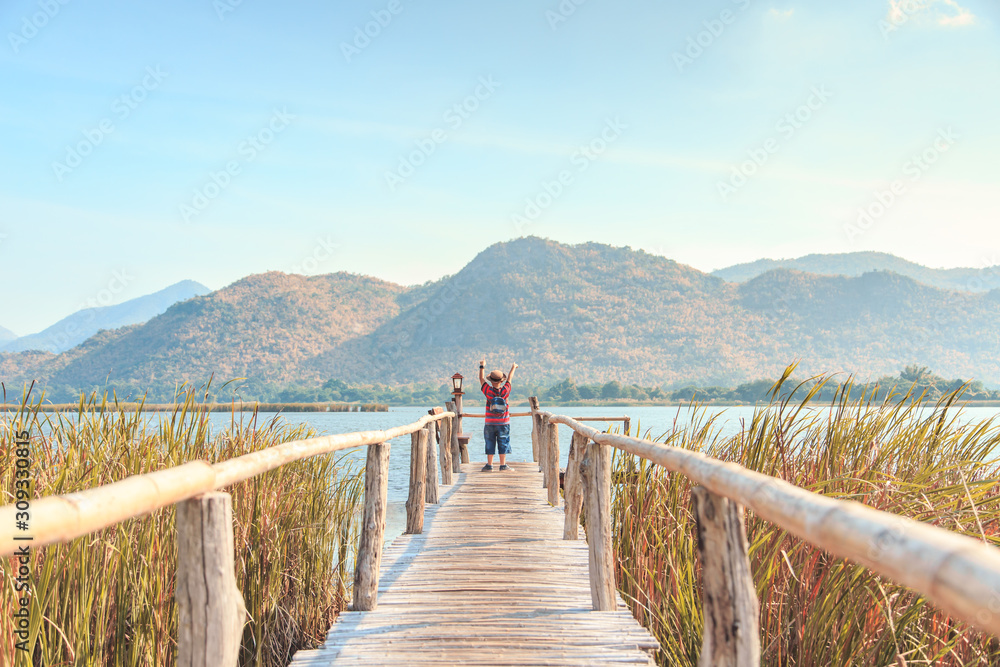 Obraz premium Boy walking on a bamboo bridge Feel fresh and freedom. at the end of the bridge in front of the dam and the mountains before sunset.