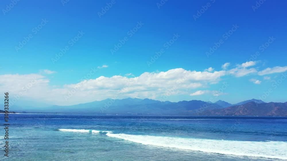 Vivid colors of sunrise with bright blue sky and white clouds rising behind the mountains horizon bordering blue sea with white waves foaming Vivid colors of sunrise with bright blue sky and white clouds rising behind the mountains horizon bordering blue sea with white waves foaming