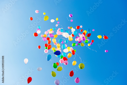 Colorful multicolored inflatable balls fly in air against background blue sky during festive festival. Salute in sky from colorful balloons. Happy holiday background