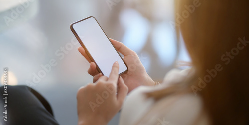 Close-up view of young businesswoman using blank screen smartphone while working on the project