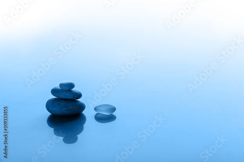 Minimalism in trend colors of the Year 2020. 3 pyramid pebbles and glass with reflections. Blue blurred background. Selective focus. Copy space.