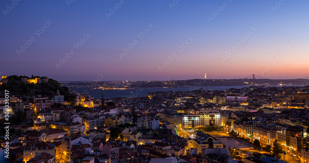 Scenic view of the downtown at dusk including Castelo de Sao Jorge, Alfama, Baixa and Bairro Alto districts, 25 de Abril Bridge over Tagus River and lit Cristo Rei monument in Lisbon, Portugal at dusk