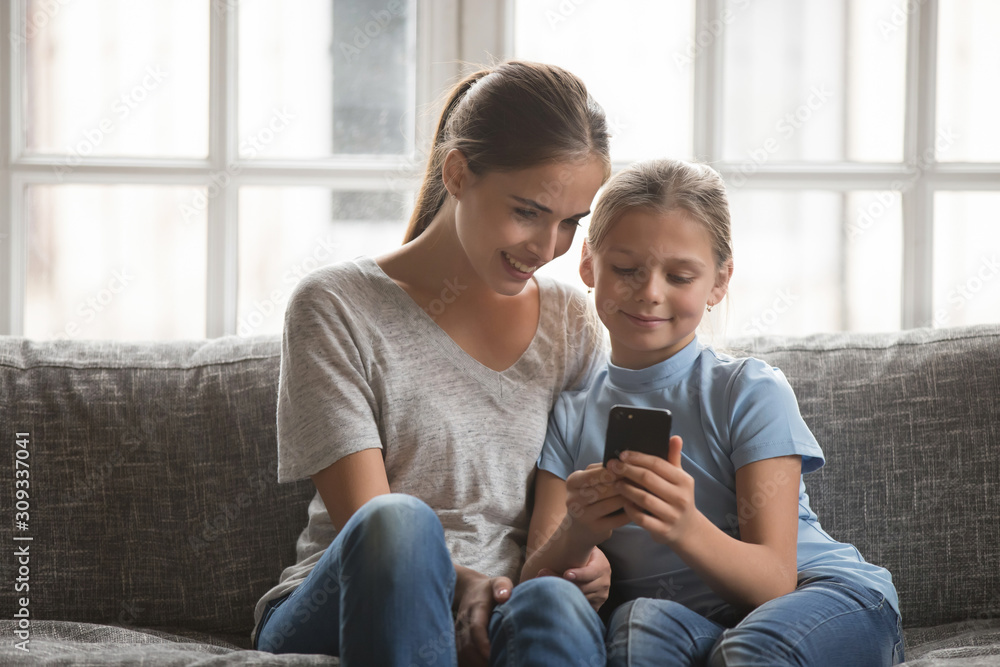 Obraz premium Smiling young mom and daughter using cellphone at home