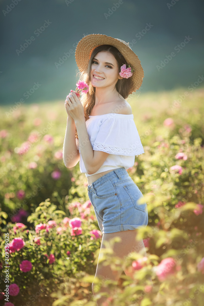 A woman in a hat walks in the summer field with a wild rose.