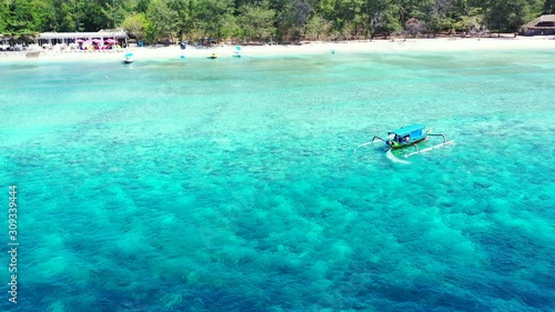 Traditional Balinese boat turning around in the crystal clear sea water near the white sandy beach photo