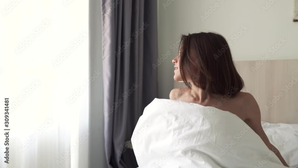 A young pretty brunette girl wakes up in bed. Girl luxuriates in a white bed. Aerial view. 4k resolution A young pretty brunette girl wakes up in bed. Girl luxuriates in a white bed. Aerial view. 4k resolution