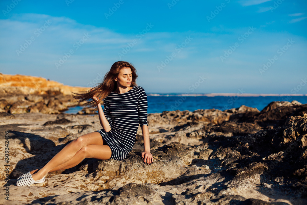 girl sits on the rocky beach enjoys sunshine girl sits on the rocky beach enjoys sunshine