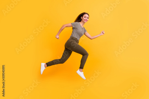 Full size profile side photo of excited enthusiastic girl jump run fast feel content candid emotions wear stylish clothes isolated over yellow color background