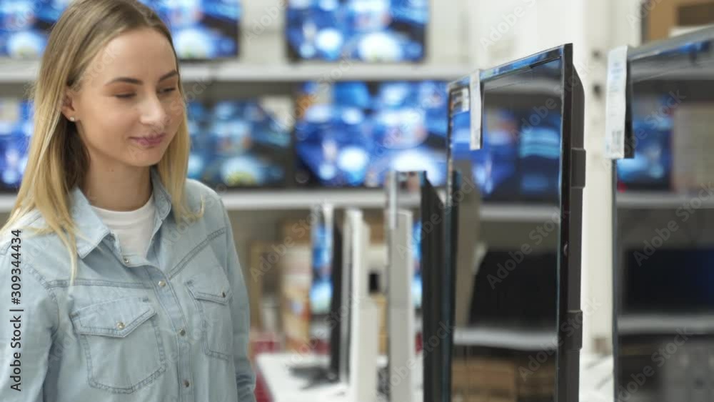 Smart modern female customer choosing large TV-sets at electronics store Smart modern female customer choosing large TV-sets at electronics store