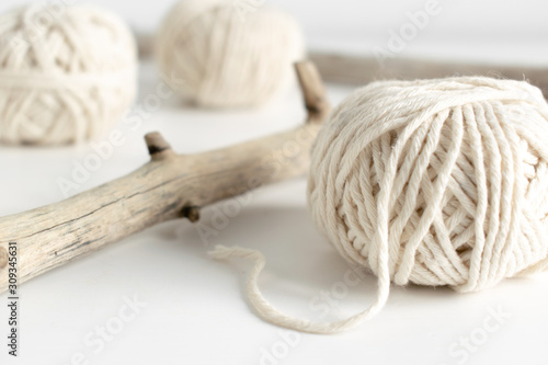 Balls of white yarn and rustic sticks on a white table. Threads of wool boho image.Good for macrame and handicrafts banners and advertisement