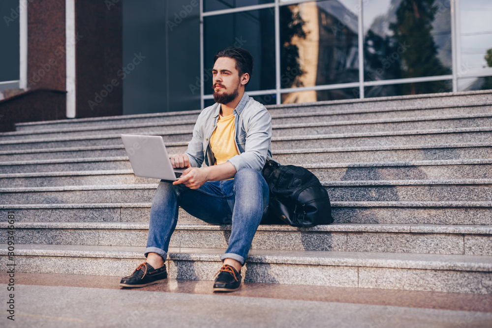 Bearded student using laptop on steps Bearded student using laptop on steps