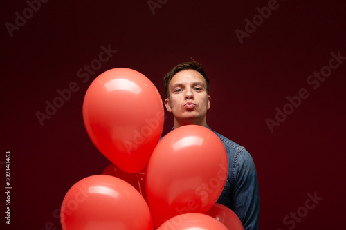 Handsome man with coral balloons isolated over dark red background. © ianachyrva