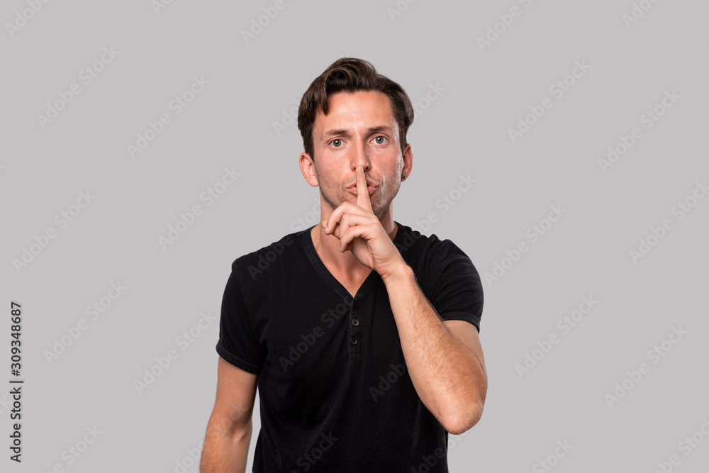 Handsome man in a black tee showing with a finger gesture to keep silence Handsome man in a black tee showing with a finger gesture to keep silence