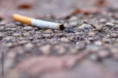 A thrown away used cigarette end with filter is lying on the ground on a footpath in winter. Seen in Bavaria, Germany in December.