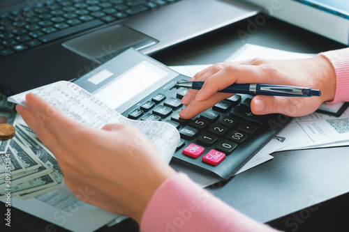 A woman accountant in the office holds a cash receipt in her hand and calculates expenses using a calculator. Market and profit analysis, tax and payment accounting, budget and money saving concept.