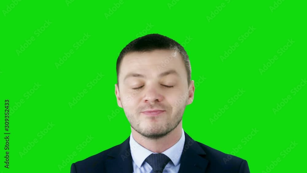 Young businessman in suit makes funny faces -grins, grimaces, sticks his tongue out, crosses his eyes, winks on green background. Chroma key Young businessman in suit makes funny faces -grins, grimaces, sticks his tongue out, crosses his eyes, winks on green background. Chroma key