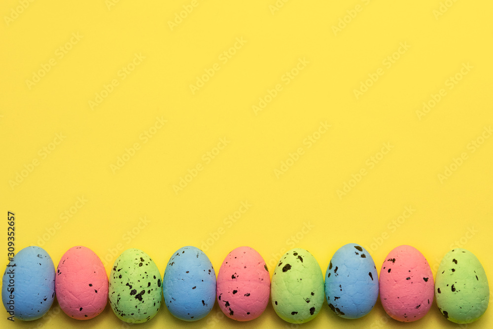 Colorful easter eggs painted in pastel colors in row on yellow background. Easter greeting card concept in trendy minimal style, copy space