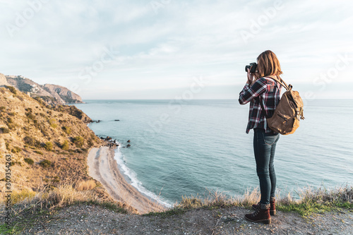 Young hip woman with a backpack exploring and photographing the coast on a beautiful day. Concept of exploration and adventures