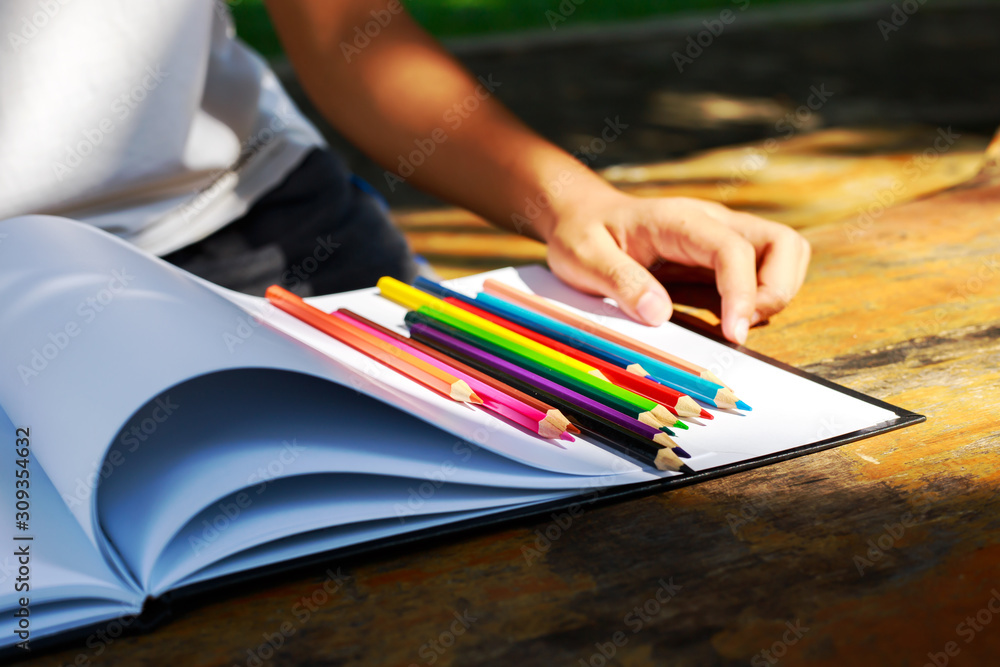 Student hand is on the wood table.The crayon is on the white paper. Student hand is on the wood table.The crayon is on the white paper.