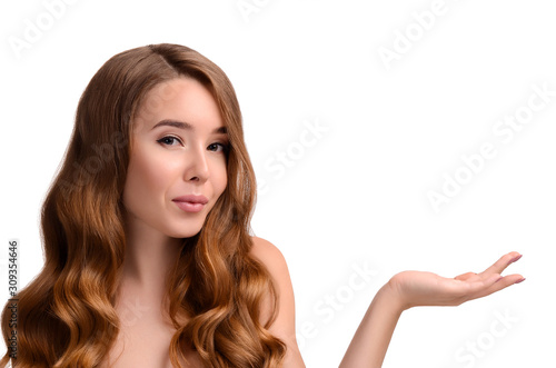 Portrait of beautiful girl with long shiny wavy hair showing product, presenting hand. Perfect Fresh Clean Skin. Youth and skin care concept. Copy space