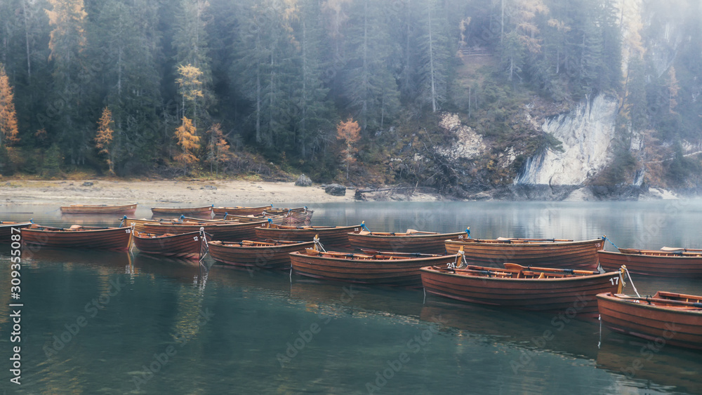 Emerald waters of Lago di Braies and wooden boats with misty forest in the background, Dolomites, Italy