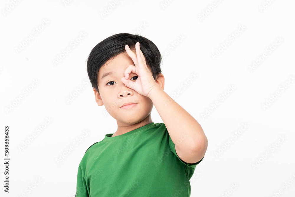 Dark haired little child with happy face smiling doing ok sign with hand on eye looking through fingers Dark haired little child with happy face smiling doing ok sign with hand on eye looking through fingers