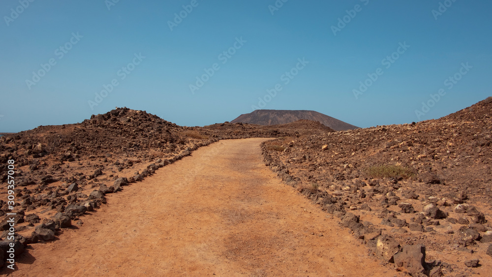 Empty path through the rough and arid landscape of Lobos Island, known locally as Isla de Lobos, a largely uninhabited islet located north of the island of Fuerteventura, Canary Islands, Spain Empty path through the rough and arid landscape of Lobos Island, known locally as Isla de Lobos, a largely uninhabited islet located north of the island of Fuerteventura, Canary Islands, Spain
