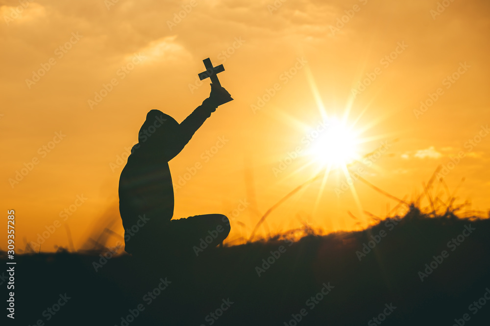 Man sit down and praying with raise the cross to sky at sunset background. christian silhouette concept.