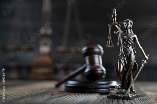 Justice concept. Themis statue and judge's gavel on the rustic wooden table and the dark background. photo