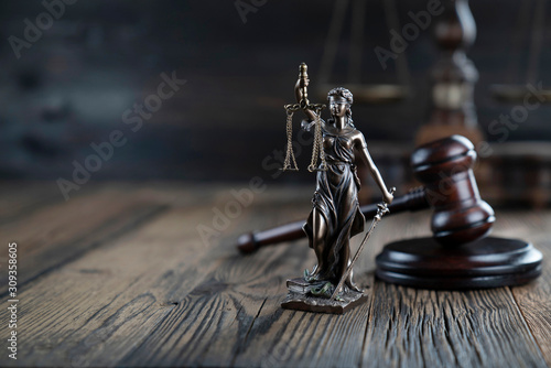 Justice concept. Themis statue and judge's gavel on the rustic wooden table and the dark background.