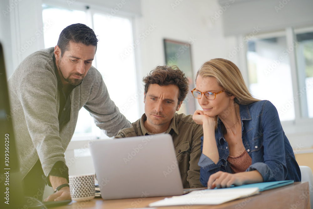 Co-workers gathering in office and using laptop Co-workers gathering in office and using laptop