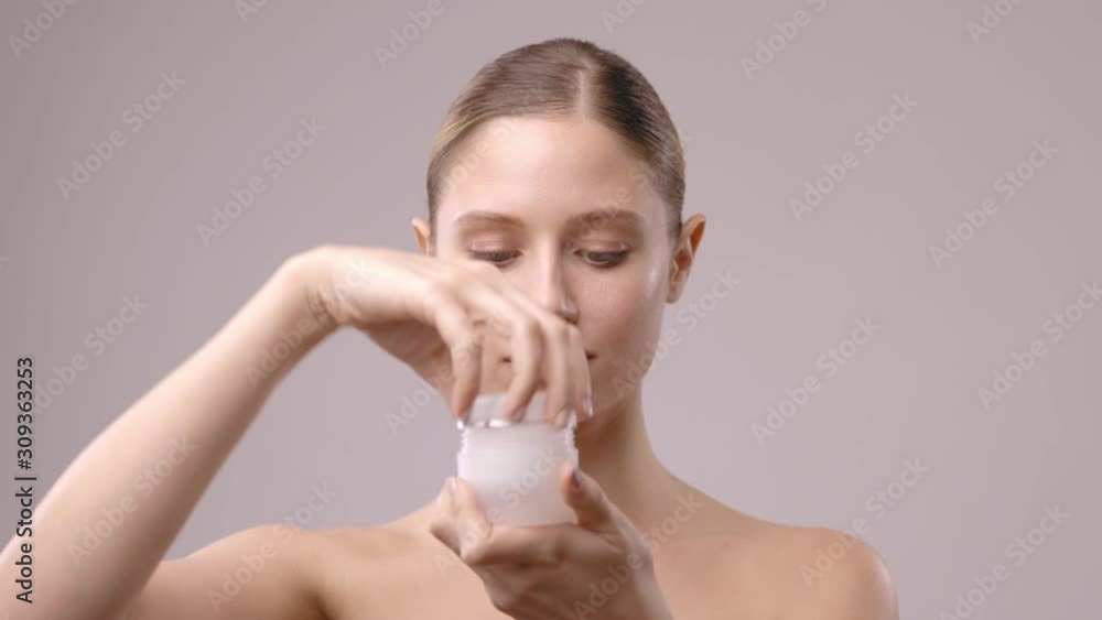 Beautiful blond young woman opening cream and putting it on her pure skin. Beautiful blond young woman opening cream and putting it on her pure skin.