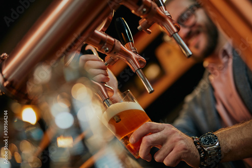 Billede på lærred Close up of handsome caucasian bearded bartender standing in bar and pouring beer from tap
