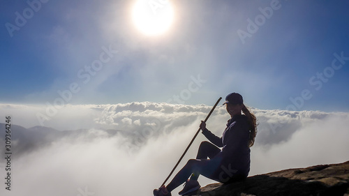 A young woman sitting on the side of volcano Inerie in Bajawa, Flores, Indonesia. She is surrounded by clouds, as if she was walking on them. Clear blue sky. Natural phenomenon. Beauty in the nature © Chris