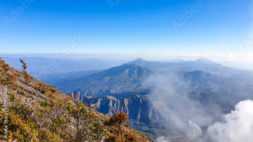 A view on volcanic island from the side of volcano Inerie in Bajawa  Flores  Indonesia. The slopes of volcano are overgrown with small plants. Few clouds below. Many volcanos in the back