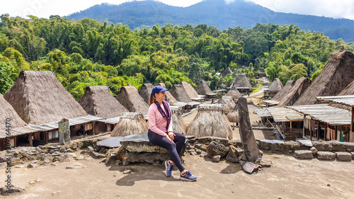 A young woman with a purple scarf admiring the Beno village in Flores, Indonesia. There are many small houses behind him. Each house is made of natural parts like wood and straw. History and tradition photo
